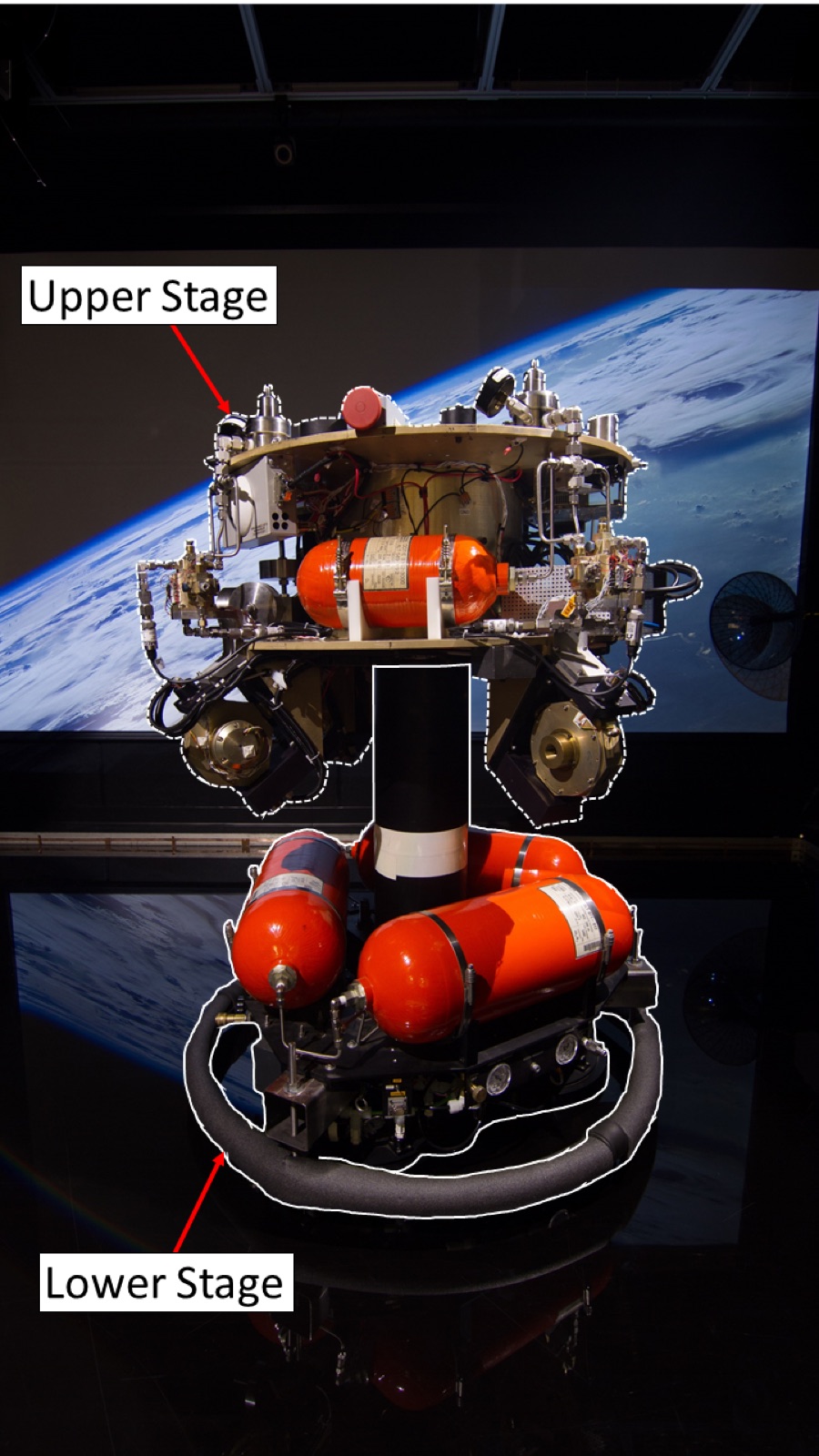 The ASTROS platform with its upper and lower stages labelled, photographed against a projected image of Earth from orbit